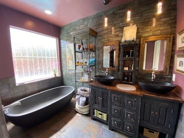 Rustic dual-vanity bathroom with stone accent wall, vessel sinks, and freestanding soaking tub — Birchard Remodeling Tucson