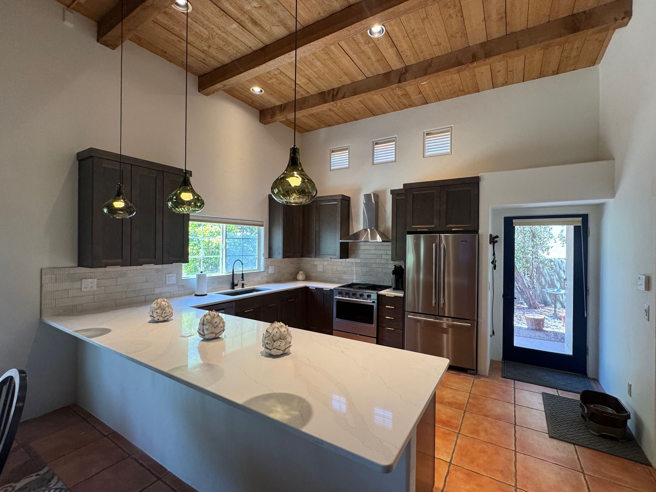 Vaulted wood ceiling kitchen with dark cabinetry, quartz island, and glass pendant lights — Birchard Remodeling Tucson